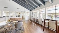 This 610 square foot space in Tucson, Arizona, showcases a blend of modern design and architectural ingenuity. The interior is dominated by a dramatic vaulted ceiling with exposed beams, painted in a contrasting grey and white scheme that adds depth and character. Large, multi-paned windows flood the area with natural light, creating an airy and spacious atmosphere.

The open-concept layout is accentuated by hardwood flooring throughout, providing a warm, cohesive look. A mezzanine level, accessible via a staircase with sleek metal railings, adds vertical interest and additional usable space. The centerpiece of the upper level is a striking circular LED lighting fixture, which serves as both a functional and artistic element.

Furnishings are minimal and modern, with a mix of seating options including bar-height tables and stools, lounge chairs, and a leather sofa. The space seamlessly blends work and relaxation areas, making it suitable for various purposes. Wall-mounted artwork, including nature-inspired pieces, adds pops of color to the predominantly neutral palette.

The kitchen area, while not fully visible, appears to be integrated into the open plan, maintaining the overall flow of the space. This versatile, contemporary design maximizes the use of the modest square footage, creating an environment that feels much larger than its actual dimensions.