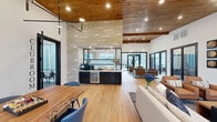 Located at 1130 Annondale Way in Fayetteville, NC, this generously sized single-floor amenity space blends contemporary design with warm, inviting elements throughout. The open-concept clubhouse area showcases soaring ceilings with rich wood beam accents and wood-paneled ceiling sections that add natural warmth, complemented by light hardwood flooring that flows seamlessly throughout.

The combined dining and living area serves as the heart of the space, featuring a striking stone accent wall, a built-in wet bar with a beverage cooler, and large glass doors that invite natural light while offering outdoor access. A separate living room provides a more intimate setting, highlighted by a dramatic tiled fireplace, large-format windows with exterior views, a wall-mounted television, and a sculptural multi-globe chandelier overhead. The dedicated dining room offers abundant natural light through wide windows and features a live-edge wood communal table.

The expansive exercise room is a standout feature, boasting soaring vaulted ceilings with exposed wood beams, light grey luxury vinyl flooring, and an impressive living moss wall installation. The fitness area is well-equipped with free weights, cable machines, cardio equipment, and a dedicated open studio area. An office rounds out the layout, providing a functional workspace within this thoughtfully designed community facility.