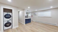 This well-appointed single-floor unit showcases a clean, modern aesthetic throughout, with light hardwood flooring and neutral-toned walls creating a bright and cohesive atmosphere. The open-concept layout connects the living area to the kitchen, maximizing the sense of space and encouraging easy movement between areas. Recessed lighting illuminates the main living zone, which also benefits from natural light through windows fitted with white blinds. A wall-mounted air conditioning unit and baseboard heating ensure year-round comfort.

The kitchen is a standout feature, boasting white shaker-style cabinetry with gold hardware, a striking blue hexagonal tile backsplash, crisp white countertops, and a full suite of stainless steel appliances including a range, over-the-range microwave, dishwasher, and refrigerator. A navy blue peninsula with pendant lighting above defines the kitchen's boundary with the open living space, adding a bold design accent.

The bedroom offers hardwood flooring, a ceiling fan, a window for natural light, and convenient closet access. The bathroom is finished with neutral tile flooring, a grey vanity with a white countertop, and a mirror, delivering a clean and functional space. Overall, the unit presents a polished, move-in-ready interior with thoughtful finishes throughout.