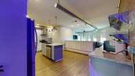 Located at 213 Chenango St in Binghamton, NY, this single-floor unit blends industrial character with modern design throughout its well-appointed layout. The heart of the space is a generously sized open-concept kitchen, which features white shaker cabinetry extending to the ceiling, granite countertops, stainless steel appliances including a gas range and refrigerator, and a central island with a bold purple accent base and pendant lighting above. Exposed ductwork runs across the ceiling, adding an urban, loft-inspired aesthetic that carries into the adjacent living area. The living room is bright and welcoming, with multiple windows allowing natural light to fill the space, a ceiling fan overhead, and ample room for comfortable seating. Hardwood-style flooring runs consistently through the main living areas, contributing to a warm and cohesive feel. The bedrooms are calm and understated, finished in soft, neutral tones with natural light from street-facing windows. The bathrooms are well-finished, offering marble-look tile flooring, a white vanity with stone countertops, and a full shower. A second bathroom features a dark-toned floating vanity and tile flooring. The overall space offers a thoughtful balance of contemporary style and functional living.