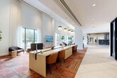 Located at 501 NW Seventh Ave in Fort Lauderdale, FL, this expansive single-floor amenity and leasing space offers a thoughtfully curated environment that blends functionality with artistic flair. The layout spans a generous footprint and includes 14 distinct areas, among them two dedicated private offices and a variety of multi-use common spaces.

The main lobby commands immediate attention with soaring double-height ceilings, floor-to-ceiling windows dressed in sheer white drapery, and an abundance of natural light that floods the interior. A long, light wood workstation anchors the leasing area, outfitted with computer workstations, pendant globe lighting, and warm cognac leather seating. Vibrant, patchwork-style area rugs in rich jewel tones define each zone, contrasting beautifully with large-format white tile flooring.

A lounge area features a curved cream sectional sofa, eclectic accent chairs, and a bold teal abstract area rug, with sliding glass doors opening to an outdoor terrace. A gallery corridor showcases framed black-and-white photography mounted on deep teal accent walls, alongside a large-scale colorful mural that energizes the space. A wood-paneled ceiling section adds warmth to the mailroom area. Private glass-walled offices offer an intimate, contemporary work setting. Throughout, lush indoor plants and curated artwork reinforce an inviting, design-forward atmosphere.