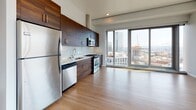 This contemporary high-rise residence is designed with clean lines, a neutral palette, and thoughtful finishes throughout. The entry opens through a solid dark-wood door into a bright hallway with light hardwood-style flooring, recessed lighting, and a sliding barn-style interior door, setting a refined tone for the space.

The open-concept kitchen is a standout feature, showcasing rich dark wood cabinetry that extends floor to ceiling, complemented by a glass subway tile backsplash and light countertops. A full suite of stainless steel appliances—including a gas range, built-in microwave, dishwasher, and refrigerator—anchors the space, which flows seamlessly into the living area. Floor-to-ceiling windows flood both the kitchen and living area with natural light while framing sweeping panoramic views of the surrounding urban skyline.

The bedrooms are generously proportioned, finished with plush carpeting and large windows that continue the dramatic city views, bringing the outdoors in with an abundance of natural light.

Two full bathrooms are appointed with large-format tile flooring, white subway tile tub surrounds, dark wood vanities with integrated sinks, and oversized mirrors, delivering a clean, modern aesthetic. The overall ambiance is polished, airy, and well-suited to contemporary urban living.