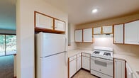 This two-floor residence offers a practical and well-organized layout across both levels. The kitchen is equipped with white cabinetry accented by warm wood trim, light countertops, a gas range, a full-size refrigerator, and a double stainless steel sink positioned beneath a window that allows natural light to brighten the space. Upper and lower cabinet storage is generously distributed throughout, providing ample room for organization.

The main living areas feature neutral-toned carpet flooring and light-colored walls, creating a clean and open atmosphere. A pass-through opening connects the kitchen area to the adjacent living space, enhancing the sense of openness. Sliding glass doors on the main level lead to an outdoor patio with views of surrounding greenery, while an upper-level room features its own sliding door opening to a balcony overlooking lush outdoor scenery.

The lower level includes a spacious carpeted room with a staircase, recessed lighting, and an interior door, offering flexible use as additional living or recreational space. Two bathrooms serve the residence — one featuring a vanity, toilet, and in-unit laundry access, and the other with a walk-in glass shower, vanity, and tile flooring. Additional bedrooms are bright and carpeted, with windows providing natural light throughout.