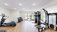 Located at 644 W Magnolia Ave in Auburn, Alabama, this fitness center offers a thoughtfully designed, single-floor layout that accommodates a comprehensive range of workout activities. The space is divided into two distinct areas, allowing users to move seamlessly between different training zones.

The main workout area features warm wood-look flooring, crisp white walls, and recessed lighting that creates a bright, clean atmosphere. Large windows and a glass door along one wall invite natural light and provide views of the outdoor surroundings, including a pool area visible from within. Structural columns accent the space while supporting an open floor plan that houses an impressive array of strength equipment, including multi-station cable machines, weight benches, and a full dumbbell rack.

A secondary room offers a more intimate setting, ideal for cardio and functional training. This area includes a spin bike, a medicine ball storage tower, and ample open floor space, complemented by a ceiling fan and a large window that brings in additional natural light.

Throughout the facility, additional equipment such as treadmills, an elliptical trainer, and a water cooler station adds to the well-rounded offerings. The overall ambiance is modern and energizing, with a clean, minimal aesthetic that keeps the focus squarely on fitness.