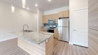 Located along the scenic Provo River Parkway in Provo, Utah, this thoughtfully designed 2-bedroom, 2-bathroom unit offers a clean, modern aesthetic across a single level. The open-concept kitchen and living area serves as the heart of the home, anchored by a striking granite-topped island with a built-in sink and sleek pendant lighting overhead. Light wood-toned cabinetry lines the kitchen walls, complemented by stainless steel appliances, a tile mosaic backsplash, and recessed lighting. Wood-look plank flooring flows throughout the main living areas, adding warmth and continuity. The living room benefits from natural light through a large window, with a ceiling fan enhancing comfort. Both bedrooms feature plush carpet and neutral wall tones, with the primary bedroom offering a spacious walk-in closet area and direct access to its en-suite bathroom. The primary bath includes wood-grain cabinetry with granite countertops, wood-look flooring, and a walk-in shower. The second bathroom mirrors the same refined finishes, featuring a full soaking tub and matching vanity details. The hallway connects all spaces efficiently, contributing to a practical and cohesive layout. The overall ambiance is bright, clean, and contemporary.