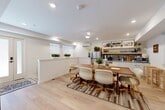 Located at 2009 N Howard St in Philadelphia, PA, this two-floor space offers a clean, modern aesthetic with warm, inviting touches throughout. Light oak hardwood flooring runs consistently across both levels, creating a sense of continuity and openness.

The lower floor features an open-plan dining and kitchen area anchored by a solid wood dining table surrounded by cushioned rolling chairs, all set atop a layered area rug. The kitchen is equipped with stainless steel appliances, white cabinetry, open wooden shelving stocked with plants and décor, and a tile backsplash. A wall-mounted mini-split unit provides climate control, and several windows with roller shades allow natural light to filter in.

The living area on this floor is a relaxed, well-appointed space featuring a plush green sofa, an organic-shaped glass coffee table, and a large modular shelving unit that serves as both storage and a room divider. A striking exposed concrete accent wall adds an industrial contrast to the otherwise soft, white interior.

The full bathroom is finished with large-format gray tile flooring, a soaking tub, a separate shower with a decorative curtain, and framed botanical artwork. The space also includes a closet and two staircases connecting the floors, ensuring smooth circulation throughout. The overall ambiance is modern, cozy, and carefully curated.