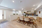 Located at 2009 N Howard St in Philadelphia, PA, this two-floor space offers a clean, modern aesthetic with warm, inviting touches throughout. Light oak hardwood flooring runs consistently across both levels, creating a sense of continuity and openness.

The lower floor features an open-plan dining and kitchen area anchored by a solid wood dining table surrounded by cushioned rolling chairs, all set atop a layered area rug. The kitchen is equipped with stainless steel appliances, white cabinetry, open wooden shelving stocked with plants and décor, and a tile backsplash. A wall-mounted mini-split unit provides climate control, and several windows with roller shades allow natural light to filter in.

The living area on this floor is a relaxed, well-appointed space featuring a plush green sofa, an organic-shaped glass coffee table, and a large modular shelving unit that serves as both storage and a room divider. A striking exposed concrete accent wall adds an industrial contrast to the otherwise soft, white interior.

The full bathroom is finished with large-format gray tile flooring, a soaking tub, a separate shower with a decorative curtain, and framed botanical artwork. The space also includes a closet and two staircases connecting the floors, ensuring smooth circulation throughout. The overall ambiance is modern, cozy, and carefully curated.