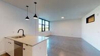 Located at 1407 C St in Vancouver, Washington, this contemporary single-floor unit showcases a thoughtfully designed modern interior with clean lines and a cohesive aesthetic throughout. Polished concrete floors run continuously across the living spaces, reflecting natural light and lending an industrial-chic character to the home.

The open-concept kitchen serves as a functional centerpiece, equipped with stainless steel appliances including a gas range and microwave, white flat-front cabinetry, open wood shelving, and a striking hexagonal tile backsplash. A central island with a light quartz countertop and a matte black sink fixture provides additional workspace and a natural gathering point. Pendant lighting with black industrial-style fixtures hangs above, complementing the kitchen's modern palette.

The living area is bright and open, benefiting from large, black-framed windows that frame outdoor views of the surrounding Vancouver neighborhood and fill the space with natural light. The crisp white walls and polished floors amplify the airy feel of the room.

A well-appointed bathroom features a long white vanity with quartz countertop, built-in shelving niches, matte black hardware, and a walk-in shower enclosed by a glass panel and adorned with a bold hexagonal tile pattern in white and grey tones. Additional storage is provided through a walk-in closet and a hallway closet, both with built-in rods and shelving. A sliding barn door adds a stylish architectural accent to the interior hallway.