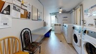 Located at 30 Campbell Crt in Stratford, Ontario, this shared laundry facility offers a practical and functional space designed to meet residents' everyday needs. The room features a lineup of commercial-grade Huebsch front-loading washing machines and matching dryers, including both stacked and standalone units, providing ample capacity for multiple users. The machines are card- or coin-operated and clearly numbered for easy identification.

The space is finished with durable vinyl tile flooring and white painted walls, maintaining a clean and utilitarian appearance throughout. A window along one wall allows natural light to brighten the interior while also providing ventilation, complemented by exposed overhead ductwork that contributes to the room's practical character. A ceiling light fixture ensures adequate illumination.

A built-in laminate folding table runs along one wall, offering a convenient surface for sorting and folding laundry. Seating is available nearby, allowing residents to wait comfortably. A bulletin board mounted on the wall displays notices and community information, adding a communal touch to the space. The room is accessed through a standard door and is well-organized to accommodate efficient use by multiple residents. Overall, this laundry facility is thoughtfully equipped to serve the building's residents with convenience and reliability.