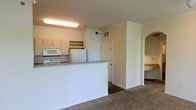 This single-floor residence offers a well-organized and functional layout designed to maximize everyday living. The kitchen serves as a central hub of the home, equipped with white appliances including a refrigerator, range, and over-the-range microwave. A raised peninsula counter creates a natural division between the kitchen and the adjacent living area, providing both additional workspace and a casual dining or gathering spot. Upper cabinetry offers ample storage, and a mounted wine rack adds a practical decorative touch above the counter space.

The flooring transitions thoughtfully throughout the unit, with hard flooring in the kitchen and utility areas giving way to plush carpeting in the living spaces, adding warmth and comfort underfoot. Crown molding runs along the upper walls, lending the space a classic and polished finish.

A dedicated in-unit laundry area is conveniently positioned just off the kitchen, with a full-size washer and dryer included. A white paneled door leads to additional storage or utility access nearby.

An elegant arched entryway connects the main living area to a secondary space, offering a glimpse of additional countertop surfaces beyond. The neutral wall tones and consistent white trim throughout create a clean, cohesive aesthetic that feels bright and welcoming across the entire floor plan.