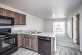 This single-floor unit is thoughtfully laid out with an open-concept design that seamlessly connects the kitchen and living area. The kitchen is well-equipped with dark-stained wood cabinetry, light countertops, and a full suite of black Whirlpool appliances, including a refrigerator, electric range, microwave, and dishwasher. Wood-look plank flooring runs throughout the kitchen, adding warmth and durability. A peninsula with an integrated sink and additional cabinetry faces the living area, enhancing the open flow between spaces.

The living area is generously sized with neutral carpet and features a sliding glass door with vertical blinds, allowing natural light to filter in while providing access to an outdoor area. The bedrooms are carpeted and finished with neutral tones, each featuring windows with blinds that bring in additional natural light.

The bathroom is clean and functional, featuring wood-look flooring, a shower-tub combination, toilet, and a dark wood vanity. A closet adjacent to the bathroom provides convenient storage. Throughout the unit, flush-mount ceiling fixtures provide consistent lighting, and the neutral color palette creates a cohesive, move-in-ready atmosphere.