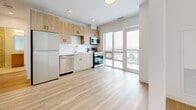 This thoughtfully designed 1-bedroom, 1-bathroom unit offers a bright and contemporary living experience across a single floor. The open-concept kitchen and living area forms the heart of the space, bathed in natural light streaming through large floor-to-ceiling windows and a glass sliding door that frames expansive urban views. Light-toned hardwood flooring runs continuously throughout, enhancing the clean, modern aesthetic.

The kitchen is well-appointed with light wood cabinetry, a herringbone-patterned tile backsplash, quartz countertops, and a full suite of stainless steel appliances including a refrigerator, dishwasher, electric range, and microwave. The living area flows seamlessly from the kitchen, creating an airy, versatile space.

The bedroom is a comfortable, sunlit retreat featuring a large corner window with sweeping city views and a sliding closet door for ample storage. A hallway connects the key areas of the unit and conveniently houses an in-unit stacked washer and dryer.

The bathroom is elegantly finished with large-format marble-look floor tiles, a glass-enclosed corner shower with matching wall tiles, a wood-toned vanity, and a mirror. The overall palette of whites and natural wood tones gives the unit a cohesive, contemporary character.