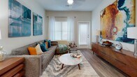 This thoughtfully designed single-floor residence offers a cohesive blend of modern finishes and functional living spaces throughout. The open-concept layout connects the kitchen and living area seamlessly, creating an inviting, airy atmosphere complemented by warm hardwood-style flooring that flows throughout the unit.

The kitchen is a standout feature, equipped with a full suite of stainless steel appliances including a gas range, microwave, and refrigerator. Rich, dark-toned cabinetry provides ample storage, while the expansive white quartz peninsula with bar seating and pendant lighting overhead makes it ideal for both casual dining and entertaining. Track lighting adds a contemporary touch to the space.

The living room is bright and welcoming, featuring large windows dressed with horizontal blinds and sheer white curtains that allow natural light to filter through. A private door leads outdoors, further enhancing the sense of openness.

The bedroom continues the warm aesthetic with hardwood-style flooring, a large window framed by sheer curtains, and ample space for furnishings including a dresser and bed.

The bathroom is finished with elegant marble-style tile flooring, dark wood vanity cabinetry, white quartz countertops, and a well-lit mirror — a clean and sophisticated retreat.

Completing the unit is a dedicated laundry closet housing a full-size side-by-side washer and dryer, with overhead wire shelving for added storage convenience.