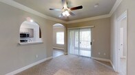 This one-bedroom, one-bathroom single-floor residence offers a well-designed layout that maximizes functionality and comfort. The living area is finished with plush carpeting and features elegant crown molding along the ceiling, adding a refined architectural detail to the space. A ceiling fan with integrated lighting provides both comfort and illumination throughout the room.

Natural light flows generously into the living area through a large sliding glass door fitted with vertical blinds, offering access to an outdoor view framed by surrounding greenery. The arched doorways connecting the living space to the bedroom and other areas lend a classic, welcoming character to the interior design.

The kitchen is accessible via a pass-through counter visible from the living area, creating a semi-open connection between the two spaces while maintaining distinct zones. Neutral-toned walls throughout complement the warm carpeting, contributing to a cohesive and understated aesthetic.

Overall, this residence balances practical living with thoughtful design details, including architectural archways, ample natural light, and a seamless indoor-outdoor connection through the sliding door.