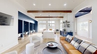Located at 11925 Jones Rd in Houston, TX, this thoughtfully designed single-story space blends modern aesthetics with functional versatility. The open-concept layout is anchored by soaring ceilings adorned with rich, exposed wood beams that add warmth and architectural character throughout. Light hardwood flooring flows seamlessly from one area to the next, reinforcing the sense of connected, expansive space.

The lounge area features a curated seating arrangement with a cognac leather sofa, rounded upholstered chairs, and a low circular coffee table, all positioned beside oversized windows that frame views of an outdoor patio equipped with seating and grilling amenities. Natural light fills the interior throughout the day.

A central island with a crisp white surface and warm wood base serves as a social hub, complete with leather bar stools and a cluster of dramatic black pendant lights overhead. Adjacent navy cabinetry, open shelving with brass accents, and a beverage station provide both style and convenience.

Bold navy shiplap-clad nooks house built-in workstations, creating dedicated co-working areas with focused lighting. Arched doorways with navy-painted tray ceilings add refined architectural detail, connecting zones with elegant transitions. A wall-mounted television and direct exterior access further enhance the space's functionality and welcoming atmosphere.