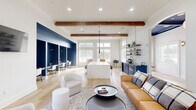 Located at 11925 Jones Rd in Houston, TX, this thoughtfully designed single-story space blends modern aesthetics with functional versatility. The open-concept layout is anchored by soaring ceilings adorned with rich, exposed wood beams that add warmth and architectural character throughout. Light hardwood flooring flows seamlessly from one area to the next, reinforcing the sense of connected, expansive space.

The lounge area features a curated seating arrangement with a cognac leather sofa, rounded upholstered chairs, and a low circular coffee table, all positioned beside oversized windows that frame views of an outdoor patio equipped with seating and grilling amenities. Natural light fills the interior throughout the day.

A central island with a crisp white surface and warm wood base serves as a social hub, complete with leather bar stools and a cluster of dramatic black pendant lights overhead. Adjacent navy cabinetry, open shelving with brass accents, and a beverage station provide both style and convenience.

Bold navy shiplap-clad nooks house built-in workstations, creating dedicated co-working areas with focused lighting. Arched doorways with navy-painted tray ceilings add refined architectural detail, connecting zones with elegant transitions. A wall-mounted television and direct exterior access further enhance the space's functionality and welcoming atmosphere.