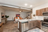 This single-floor residence offers a well-designed open-concept layout that seamlessly connects the living, dining, and kitchen areas. The living room is a comfortable and stylish gathering space, featuring wood-style flooring, ceiling fans, and exposed ductwork that adds an industrial touch to the interior. The kitchen is fully equipped with stainless steel appliances — including a refrigerator, range, microwave, and dishwasher — complemented by rich dark-toned cabinetry, granite countertops, and a tile backsplash. A kitchen island with seating provides a casual dining option, while a dedicated dining area offers additional space for meals. Both bedrooms are carpeted for comfort, each featuring ceiling fans and ample closet storage. Natural light filters through the windows, creating a bright and welcoming atmosphere. The bathroom includes a dark wood vanity with a granite countertop, a large mirror, and wood-style flooring, offering a clean and functional design. A dedicated in-unit laundry room houses a full-size washer and dryer, along with overhead shelving for extra storage. The overall ambiance of the space balances modern convenience with a warm, residential aesthetic.