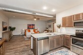 This single-floor residence offers a well-designed open-concept layout that seamlessly connects the living, dining, and kitchen areas. The living room is a comfortable and stylish gathering space, featuring wood-style flooring, ceiling fans, and exposed ductwork that adds an industrial touch to the interior. The kitchen is fully equipped with stainless steel appliances — including a refrigerator, range, microwave, and dishwasher — complemented by rich dark-toned cabinetry, granite countertops, and a tile backsplash. A kitchen island with seating provides a casual dining option, while a dedicated dining area offers additional space for meals. Both bedrooms are carpeted for comfort, each featuring ceiling fans and ample closet storage. Natural light filters through the windows, creating a bright and welcoming atmosphere. The bathroom includes a dark wood vanity with a granite countertop, a large mirror, and wood-style flooring, offering a clean and functional design. A dedicated in-unit laundry room houses a full-size washer and dryer, along with overhead shelving for extra storage. The overall ambiance of the space balances modern convenience with a warm, residential aesthetic.