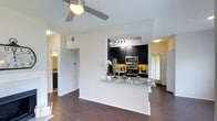 Located at 4405 Waterford Valley Dr in Durham, North Carolina, this single-floor residence offers a thoughtfully designed open-concept layout that seamlessly connects the living and kitchen areas. The kitchen is a standout feature, showcasing dark espresso cabinetry, granite countertops, and a full suite of stainless steel appliances including a refrigerator, microwave, and electric range. A peninsula counter extends into the living space, creating an ideal area for casual dining or entertaining. Track lighting above the kitchen adds focused illumination, complementing the natural light that filters in through slatted blinds. The living area is anchored by rich, dark hardwood-style flooring that runs throughout the space, adding warmth and visual continuity. A ceiling fan with integrated lighting keeps the area comfortable and well-lit. Crisp white walls and an accent of bold yellow in the kitchen backsplash area provide a lively contrast to the dark cabinetry. Hallways branch off from the main living area, offering access to additional rooms including what appears to be a bathroom and bedroom. The overall ambiance is modern and functional, balancing contemporary finishes with a comfortable, livable aesthetic well-suited to everyday life in Durham.