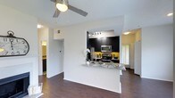 Located at 4405 Waterford Valley Dr in Durham, North Carolina, this single-floor residence offers a thoughtfully designed open-concept layout that seamlessly connects the living and kitchen areas. The kitchen is a standout feature, showcasing dark espresso cabinetry, granite countertops, and a full suite of stainless steel appliances including a refrigerator, microwave, and electric range. A peninsula counter extends into the living space, creating an ideal area for casual dining or entertaining. Track lighting above the kitchen adds focused illumination, complementing the natural light that filters in through slatted blinds. The living area is anchored by rich, dark hardwood-style flooring that runs throughout the space, adding warmth and visual continuity. A ceiling fan with integrated lighting keeps the area comfortable and well-lit. Crisp white walls and an accent of bold yellow in the kitchen backsplash area provide a lively contrast to the dark cabinetry. Hallways branch off from the main living area, offering access to additional rooms including what appears to be a bathroom and bedroom. The overall ambiance is modern and functional, balancing contemporary finishes with a comfortable, livable aesthetic well-suited to everyday life in Durham.