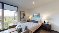 Located in the vibrant Williams Avenue corridor of Portland, Oregon, this contemporary studio unit offers a thoughtfully designed open-concept layout across a single floor. The space is anchored by a wall of floor-to-ceiling windows that flood the interior with natural light and frame sweeping treetop views of the surrounding neighborhood.

The kitchen is outfitted with dark espresso cabinetry extending to the ceiling, white quartz countertops with a classic subway tile backsplash, and a full suite of stainless steel appliances including a gas range, dishwasher, and microwave. The galley-style configuration maximizes efficiency while maintaining a sleek, modern aesthetic.

The open living and sleeping area flows seamlessly from the kitchen, with hardwood-style flooring running throughout. Large windows continue into this space, reinforcing the connection to the outdoors. A dedicated closet provides organized storage, and recessed lighting adds to the clean, contemporary feel.

The bathroom features dark wood vanity cabinetry with a white countertop, complementing the consistent design language found throughout the unit. A bold panel-style door adds an architectural accent at the entry.

Overall, the unit presents a refined, modern aesthetic with high-quality finishes and an emphasis on natural light and outdoor connectivity.