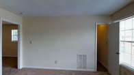 Located at 3835 Guess Rd in Durham, North Carolina, this single-floor residence offers a straightforward and functional layout designed for comfortable everyday living. The interior is finished with neutral, warm beige walls that create a clean and inviting atmosphere throughout. The main living area is carpeted, providing a soft underfoot feel, and is kept comfortable year-round by a wall-mounted HVAC vent integrated seamlessly into the baseboard. A textured ceiling adds a subtle visual layer to the space, while bright white trim and baseboards provide crisp contrast against the warm wall tones. The open wall space offers versatile opportunities for furniture arrangement and personalization. A doorway leads to an adjacent room, hinting at a connected and accessible floor plan. The overall ambiance is calm and neutral, making it a blank canvas well-suited for a variety of interior styles. The single-floor design ensures easy accessibility throughout the home, and the practical finishes reflect a focus on low-maintenance, functional living. This Durham property presents a solid foundation for those looking to settle into a no-fuss, move-in ready space.