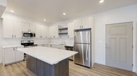 This well-designed 2-bedroom, 1-bathroom residence offers a thoughtful single-level layout with modern finishes throughout. The open-concept kitchen and living area serves as the heart of the home, anchored by a striking kitchen island with a dark wood-panel base and crisp white quartz countertop. The kitchen is outfitted with white shaker-style cabinetry, open floating shelves, a full suite of stainless steel appliances including a refrigerator, microwave, dishwasher, and range, along with a clean white subway tile backsplash. Light wood-look plank flooring extends throughout the main living areas, enhancing the bright, airy feel created by recessed lighting and large windows with vertical blinds that invite natural light into the living space. Both bedrooms are carpeted for comfort, with clean white walls and window treatments providing a calm, neutral atmosphere. The primary bedroom offers a generous footprint with ample room for furnishings. The bathroom features a wide vanity with white countertop, an undermount sink, a large mirror, and a clean, minimalist design. A connecting hallway provides practical access between all rooms, completing this efficiently designed and move-in-ready residence.