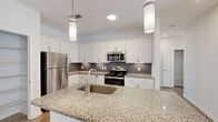 Located at 327 Guinevere Ln in Wilmington, NC, this single-floor home offers a thoughtfully designed layout with modern finishes throughout. The kitchen is a standout feature, showcasing white shaker-style cabinetry, granite countertops, a dark subway tile backsplash, and a full suite of stainless steel appliances including a refrigerator, gas range, microwave, and dishwasher. A large center island with an undermount sink and pendant lighting above makes this space both functional and visually appealing. Light wood-look flooring flows through the main living areas, complementing the clean, neutral color palette. The living spaces are bright and open, benefiting from natural light streaming through windows with slatted blinds and ceiling fans for added comfort. Bedrooms feature plush carpeting, ceiling fans, and ample natural light. The bathroom is finished with matching granite-top white vanities, light wood flooring, and accessible grab bars, with a window providing natural light. Additional storage is available through a well-organized walk-in closet with built-in shelving. Throughout the home, crisp white panel doors, clean trim work, and a cohesive neutral palette create a fresh, move-in-ready atmosphere.