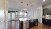 This well-appointed 3-bedroom, 3-bathroom single-floor residence in Southside Place, TX offers a thoughtfully designed layout with high-end finishes throughout. The open-concept kitchen serves as the heart of the home, showcasing dark cabinetry, granite countertops, a large center island, a stainless steel farmhouse sink, pendant lighting, a decorative brick tile backsplash, and stainless steel appliances including a built-in wine cooler. Rich hardwood flooring extends through the main living and kitchen areas, complemented by an abundance of natural light pouring through large windows and ceiling fans in every room. The spacious living area features floor-to-ceiling windows with exterior access, creating a bright and airy atmosphere. Each bedroom is carpeted for comfort, with ceiling fans and windows providing ventilation and natural light. The primary suite includes a generously sized walk-in closet with built-in shelving and hanging rods. The bathrooms are finished with granite vanity countertops, dark cabinetry, tile flooring, and a soaking tub with tiled surround. Two closets provide ample storage throughout the home, making this residence both functional and elegant.