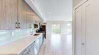 This modern studio in Troy, Michigan offers a thoughtfully designed open-concept layout that seamlessly integrates the kitchen and living area into a single, cohesive living space. Light wood-tone flooring flows throughout, complementing the neutral gray walls and crisp white trim to create a bright, contemporary atmosphere.

The kitchen is a standout feature, outfitted with two-tone cabinetry — warm wood upper cabinets paired with lighter lower units — accented by gold-toned hardware. A white quartz countertop runs the length of the galley-style kitchen, paired with a glossy subway tile backsplash. Stainless steel appliances, including a gas range, microwave, refrigerator, and dishwasher, complete the functional and stylish setup.

The living area is filled with natural light from large sliding glass doors that open onto a private balcony with outdoor views, accompanied by an additional side window. Recessed lighting adds warmth throughout the space. A double-door closet provides practical storage.

The bathroom features large-format tile flooring, a walk-in glass-enclosed shower with floor-to-ceiling tile surround, a wood-toned vanity, and clean, modern fixtures — delivering a spa-like finish. This studio offers a polished, move-in-ready living experience in a well-appointed package.