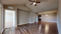 This single-story home is designed with a cohesive, modern aesthetic and a functional open layout. The living area is a standout space, featuring soaring vaulted ceilings with a ceiling fan and wood-style flooring that extends throughout the main areas. A built-in niche adds a decorative architectural detail, while an open sightline connects the living space directly to the kitchen and dining area, which is illuminated by an elegant chandelier.

The kitchen is well-equipped with dark espresso cabinetry, granite-style countertops, a classic white subway tile backsplash, and a full suite of stainless steel appliances including a refrigerator, range, microwave, and dishwasher. Ample cabinet storage lines both sides of the kitchen, maximizing functionality.

A hallway adorned with crown molding and white panel doors connects the private areas of the home. The bedrooms feature plush carpet, ceiling fans, and natural light from windows. One bedroom includes access to a spacious walk-in closet outfitted with wire shelving on multiple walls.

The primary bathroom offers a dual-sink vanity with dark cabinetry, granite countertops, a large mirror, and hardwood-style flooring, with direct access to the adjoining bedroom. Throughout, neutral gray tones and clean white trim create a polished, move-in-ready atmosphere.
