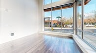 This thoughtfully designed 2-bedroom, 1-bathroom residence delivers a modern living experience across a single level of well-proportioned space. The open-concept kitchen and living area serves as the heart of the home, featuring dramatic soaring ceilings that amplify the sense of volume and airiness. Expansive floor-to-ceiling windows flood the living area with abundant natural light while framing street-level views of the surrounding neighborhood.

The kitchen is outfitted with contemporary two-tone cabinetry — combining white upper cabinets with warm wood-grain lower cabinets — complemented by a classic subway tile backsplash, light quartz countertops, and a full suite of stainless steel appliances including a refrigerator, electric range, built-in microwave, and dishwasher. Wood-look plank flooring runs throughout the main living areas, adding warmth and cohesion.

The primary bedroom is generously sized, featuring large windows that invite natural light and an open closet for convenient storage. Bedrooms are finished with soft carpeting for added comfort. The bathroom offers a clean, modern aesthetic with a wood-grain vanity, white countertop, undermount sink, and a large mirror. The overall design palette of neutral tones, clean lines, and quality materials creates a bright, contemporary living environment.