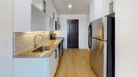 Located at Pickwick Plaza in downtown Kansas City, Missouri, this single-floor unit offers a thoughtfully designed layout with modern finishes throughout. The space features light hardwood flooring that runs continuously, contributing to a cohesive and airy feel across all areas.

The kitchen is a standout feature, designed in a galley configuration with white cabinetry accented by matte black hardware. Granite countertops, a subway tile backsplash with under-cabinet lighting, and stainless steel appliances — including a refrigerator, range, and microwave — provide both style and functionality. A window at the far end of the kitchen area allows natural light to filter in, offering views of the surrounding cityscape.

The living and sleeping areas are open and neutral in tone, with crisp white walls and generous wall space. Windows bring in additional natural light and frame exterior urban views, enhancing the sense of openness within the unit.

The bathroom is cleanly finished with large-format floor tiles, a full tub and shower combination enclosed by sliding glass doors, and white subway tile surround. The overall design maintains a consistent modern aesthetic with chrome fixtures and efficient use of space.

Throughout the unit, the clean lines, neutral palette, and contemporary finishes create a bright, functional environment well-suited to urban living in the heart of Kansas City.