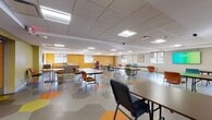 Located at 13959 Woodward Ave in Highland Park, Michigan, this single-floor community space is designed to accommodate a wide range of activities and group functions. The layout is open and expansive, offering generous floor space that can be arranged to suit various event formats, from seated presentations to casual gatherings.

The flooring is a standout design element, featuring a bold hexagonal tile pattern in shades of orange, yellow, and gray that adds visual energy throughout the space. Walls are painted in warm accent colors—including mustard yellow and olive green—creating a welcoming and lively atmosphere. A drop tile ceiling houses a grid of recessed fluorescent panel lights, ensuring consistent, well-distributed illumination across the entire area.

Multiple windows along the perimeter allow natural light to enter, complemented by roller shades for light control. The space includes a built-in service counter with wood-toned cabinetry, suitable for registration, refreshments, or administrative use. Colorful stackable chairs and folding tables throughout allow for adaptable configurations. A wall-mounted flat-screen television and framed artwork provide functional and aesthetic finishing touches, making this a practical and inviting multi-purpose facility.