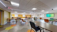 Located at 13959 Woodward Ave in Highland Park, Michigan, this single-floor community space is designed to accommodate a wide range of activities and group functions. The layout is open and expansive, offering generous floor space that can be arranged to suit various event formats, from seated presentations to casual gatherings.

The flooring is a standout design element, featuring a bold hexagonal tile pattern in shades of orange, yellow, and gray that adds visual energy throughout the space. Walls are painted in warm accent colors—including mustard yellow and olive green—creating a welcoming and lively atmosphere. A drop tile ceiling houses a grid of recessed fluorescent panel lights, ensuring consistent, well-distributed illumination across the entire area.

Multiple windows along the perimeter allow natural light to enter, complemented by roller shades for light control. The space includes a built-in service counter with wood-toned cabinetry, suitable for registration, refreshments, or administrative use. Colorful stackable chairs and folding tables throughout allow for adaptable configurations. A wall-mounted flat-screen television and framed artwork provide functional and aesthetic finishing touches, making this a practical and inviting multi-purpose facility.