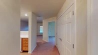 This single-floor residence offers a well-organized layout designed for comfortable, everyday living. The kitchen is a functional centerpiece, equipped with warm oak cabinetry providing generous upper and lower storage, light-toned countertops, white appliances including a coil-burner range, over-the-range microwave, dishwasher, and a stainless steel double sink. A pass-through window connects the kitchen to adjacent living areas, and light tile flooring enhances the bright, practical atmosphere.

The bedrooms are carpeted in neutral tones and receive natural light through windows framed with blue valances, offering views of surrounding greenery. Each room includes a closet with a six-panel door and maintains a clean, neutral color palette throughout.

The hallway serves as a central corridor connecting the main living areas and features plush carpeting, recessed lighting, and a large six-panel closet door offering additional storage. A wooden dresser unit is integrated into the hallway space, adding practical functionality.

The bathroom includes warm wood cabinetry with a white countertop and sink, a large mirror, and a separate water closet area with a grab bar, toilet, and glass-door shower, finished with light tile flooring. Overall, the home presents a straightforward, livable design with consistent finishes throughout.