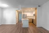 Located at 465 W San Carlos St in San Jose, CA, this well-appointed one-bedroom, one-bathroom unit offers a thoughtfully designed open-concept layout with modern finishes throughout. Warm hardwood-style flooring flows seamlessly across the entire space, complemented by crisp white walls and abundant natural light from multiple windows dressed with horizontal blinds.

The kitchen is a standout feature, showcasing a striking quartz waterfall island with an undermount sink and brushed gold faucet. Cabinetry combines sleek white upper cabinets with natural wood-toned lower cabinets, set against a marble-inspired tile backsplash. Stainless steel appliances, including a refrigerator, range, and over-the-range microwave, complete the contemporary culinary space.

The open living area is airy and bright, featuring a stylish wood-blade ceiling fan and views of surrounding greenery through large windows. The spacious bedroom offers two windows, a ceiling fan, and access to generous closet space, including a walk-in closet with wire shelving for ample storage. Additional closets throughout the hallway provide further organizational flexibility.

The bathroom is clean and functional, with wood-style flooring and a window for natural ventilation. A private balcony extends the living space outdoors, rounding out this modern San Jose residence.