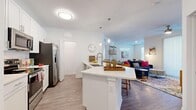 Located in Tampa, FL, this single-story, 2-bedroom, 2-bathroom residence offers a thoughtfully designed open-concept layout finished with contemporary details throughout. The kitchen serves as a central hub, featuring white shaker cabinetry, quartz countertops, a large island with bar seating, pendant lighting, and a full suite of stainless steel appliances including a refrigerator with ice maker, microwave, and range. Light wood-style flooring flows seamlessly from the kitchen into the living area, which is bright and welcoming, benefiting from natural light through large sliding glass doors that lead to a private balcony. The living space comfortably accommodates a dining area as well. Both bedrooms are carpeted and include ceiling fans and windows with blinds. The spacious primary bedroom connects to a bathroom with a walk-in glass-enclosed shower and white vanity with quartz countertops. A second full bathroom serves the additional bedroom. A dedicated laundry room houses a full-size washer. Clean white walls, consistent finishes, and a neutral palette create a cohesive, modern ambiance throughout the entire residence.