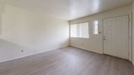 Located on Lomas Blvd NE in Albuquerque, New Mexico, this 2-bedroom, 1-bathroom residence offers a straightforward and functional layout across a single floor. The open-concept living and kitchen area forms the heart of the home, where light gray wood-style flooring runs throughout, complementing the neutral cream-toned walls. A peninsula counter separates the kitchen from the living space, providing both a visual division and additional prep surface. The kitchen is well-equipped with white cabinetry, black appliances including a gas range, refrigerator, and dishwasher, and a built-in sink with ample counter space. The living area receives natural light through a large window fitted with vertical blinds, and a wall-mounted heater unit provides efficient climate control. Both bedrooms are carpeted for comfort, with one featuring a ceiling fan and a window overlooking a greenery-filled outdoor area. A full-sized closet with bi-fold doors provides dedicated storage in the bedroom. The bathroom includes a tub-shower combination, a vanity with countertop storage, and open built-in shelving for added organization. A dedicated closet completes the unit's storage offerings, making this a practical and well-appointed residence.