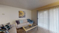 This single-floor residence offers a functional and cohesive layout, connecting the main living spaces in an efficient, open arrangement. The living room features neutral carpet flooring and a large sliding glass door fitted with vertical blinds, allowing natural light to fill the space. A glass-top coffee table and comfortable seating area make this room an inviting place to relax.

Adjacent to the living room, the dining area accommodates a round glass-top table with seating for several guests, accented by warm hardwood-style flooring and a contemporary pendant light overhead. The space flows seamlessly into the kitchen, which features warm wood cabinetry, light countertops, a peninsula with additional prep space, and white appliances including a refrigerator, range, and built-in microwave. Recessed lighting and hardwood-style flooring complete the kitchen's practical design.

The bedroom is carpeted and features a ceiling fan with integrated lighting and a window that brings in natural light. The full bathroom includes a wide vanity with a large mirror, ample cabinet storage, wood-toned cabinetry, light countertops, and a shower-tub combination. Hardwood-style flooring extends throughout the bathroom, adding a cohesive finish to the unit.
