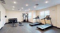 Located at 1401 Davenport Blvd in Davenport, Florida, this dedicated fitness center offers a well-appointed exercise room designed to support a well-rounded workout routine. The space is housed on a single floor and features durable rubber flooring throughout, providing both safety and functionality for a variety of exercises.

The room is equipped with multiple Spirit-brand treadmills and an elliptical trainer for cardiovascular workouts, alongside a multi-station cable machine that supports a wide range of strength-training movements. A dedicated free weights area includes a full rack of dumbbells and adjustable weight benches, accommodating users of varying fitness levels. Stability balls and resistance bands are also available, mounted neatly on a wall-mounted rack, adding versatility for functional training and flexibility work.

Natural light filters in through several windows fitted with horizontal blinds, keeping the space bright and inviting. Recessed ceiling lighting provides consistent illumination throughout. The neutral, light-toned walls contribute to an open and clean atmosphere. The layout offers ample open floor space, allowing users to move freely between equipment zones. Practical amenities such as a waste receptacle and an electrical panel are neatly integrated into the space. The fitness center is well-organized, making it a convenient and fully functional facility for daily exercise.