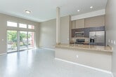 This thoughtfully designed single-floor residence at 30333 Southfield Road in Southfield, Michigan offers a contemporary open-concept layout that seamlessly connects the kitchen, dining, and living areas. The kitchen is appointed with rich dark cabinetry, granite stone countertops, a breakfast bar peninsula with an undermount sink, and a full suite of stainless steel appliances including a gas range, microwave, and refrigerator with ice dispenser. Light-toned luxury flooring runs throughout the main living areas, complementing the warm neutral wall tones and creating a bright, cohesive aesthetic. The spacious living area is anchored by large sliding glass doors topped with transom windows that flood the space with natural light and open to a private balcony overlooking the surrounding greenery. The bedroom features plush carpeting, a large picture window with outdoor views, and generous wall space. Two bathrooms serve the unit: a full bath complete with a tiled tub-shower surround, glass shower doors, and granite vanity, and a half bath with a dark-cabinet vanity and granite countertop. Recessed lighting and clean architectural lines throughout give the space a polished, modern feel well-suited for comfortable everyday living.