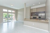 This thoughtfully designed single-floor residence at 30333 Southfield Road in Southfield, Michigan offers a contemporary open-concept layout that seamlessly connects the kitchen, dining, and living areas. The kitchen is appointed with rich dark cabinetry, granite stone countertops, a breakfast bar peninsula with an undermount sink, and a full suite of stainless steel appliances including a gas range, microwave, and refrigerator with ice dispenser. Light-toned luxury flooring runs throughout the main living areas, complementing the warm neutral wall tones and creating a bright, cohesive aesthetic. The spacious living area is anchored by large sliding glass doors topped with transom windows that flood the space with natural light and open to a private balcony overlooking the surrounding greenery. The bedroom features plush carpeting, a large picture window with outdoor views, and generous wall space. Two bathrooms serve the unit: a full bath complete with a tiled tub-shower surround, glass shower doors, and granite vanity, and a half bath with a dark-cabinet vanity and granite countertop. Recessed lighting and clean architectural lines throughout give the space a polished, modern feel well-suited for comfortable everyday living.