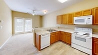 Located at 3555 Sweetwater Rd in Duluth, GA, this one-bedroom, one-bathroom unit offers a thoughtfully arranged single-floor layout. The open-concept kitchen, dining, and living area serves as the heart of the home, featuring warm oak cabinetry, light-toned countertops, and white appliances including a range, dishwasher, refrigerator, and microwave. Light hardwood-style flooring runs through the kitchen, transitioning to plush carpet in the living and bedroom areas. A ceiling fan overhead and French doors leading to a private balcony allow for natural light and outdoor access, enhancing the airy feel of the main living space. The bedroom is a comfortable, well-proportioned room with soft carpeting, a ceiling fan, and a window offering outdoor views. A dedicated closet provides ample storage. The bathroom is well-appointed with warm oak cabinetry, a tall linen tower, a white countertop vanity, a large wall mirror with overhead lighting, and a tub/shower combination. Additional utility and laundry spaces add practical convenience to the unit. Neutral warm-beige wall tones throughout create a cohesive and inviting atmosphere.