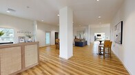 Located in Enola, PA, this expansive two-floor facility blends modern design with functional wellness spaces across an impressive footprint. Light hardwood flooring flows throughout, complementing the crisp white walls and creating a clean, contemporary aesthetic.

The centerpiece of the space is the large exercise room, which rises to soaring double-height ceilings and is flooded with natural light from an array of windows offering outdoor views. It is fully equipped with strength machines, cardio equipment, free weights, and functional training accessories. A motivational "Life Responds to Effort" wall accent reinforces the fitness-focused atmosphere. A sleek staircase with black metal railings connects the main floor to an upper-level mezzanine, where additional cardio equipment is positioned beneath vaulted ceilings and panoramic windows.

The living areas are thoughtfully designed, featuring comfortable seating arrangements, curated artwork, and warm natural light. The combined dining and living space offers a welcoming setting, while a separate sitting room with plush seating provides a more intimate lounge area. A well-appointed hallway with recessed lighting and warm wood tones connects the various spaces seamlessly. The entry area features a stylish reception-style console and large mirror, setting an elegant tone upon arrival.