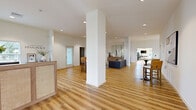 Located in Enola, PA, this expansive two-floor facility blends modern design with functional wellness spaces across an impressive footprint. Light hardwood flooring flows throughout, complementing the crisp white walls and creating a clean, contemporary aesthetic.

The centerpiece of the space is the large exercise room, which rises to soaring double-height ceilings and is flooded with natural light from an array of windows offering outdoor views. It is fully equipped with strength machines, cardio equipment, free weights, and functional training accessories. A motivational "Life Responds to Effort" wall accent reinforces the fitness-focused atmosphere. A sleek staircase with black metal railings connects the main floor to an upper-level mezzanine, where additional cardio equipment is positioned beneath vaulted ceilings and panoramic windows.

The living areas are thoughtfully designed, featuring comfortable seating arrangements, curated artwork, and warm natural light. The combined dining and living space offers a welcoming setting, while a separate sitting room with plush seating provides a more intimate lounge area. A well-appointed hallway with recessed lighting and warm wood tones connects the various spaces seamlessly. The entry area features a stylish reception-style console and large mirror, setting an elegant tone upon arrival.