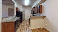Located at 1558 East Sweet Water Circle in Post Falls, Idaho, this single-floor unit offers a well-organized, open-concept layout designed for comfortable everyday living. Upon entry, the foyer transitions seamlessly into a carpeted living area, anchored by a pass-through kitchen opening that maintains visual connectivity throughout the main living space. The kitchen is generously sized, featuring rich dark wood cabinetry, laminate wood-look flooring, a full suite of black appliances including a refrigerator, range, dishwasher, and built-in microwave, along with a double basin sink and granite-toned countertops. A breakfast bar peninsula adds both function and style. The living room extends to a sliding glass door that opens to a private balcony, offering pleasant views of the surrounding neighborhood and landscape. A ceiling fan with light fixture provides comfort and circulation. The bedroom is a well-proportioned, carpeted space with a large window that fills the room with natural light and frames outdoor views. The bathroom is clean and functional, with tile flooring, a full soaking tub with shower, a vanity featuring dark wood cabinetry and stone-toned countertops, and chrome hardware. A dedicated laundry area with in-unit washer hookups adds everyday convenience to this thoughtfully designed residence.