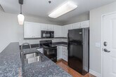 Situated along the iconic Woodward Avenue in Detroit's Midtown neighborhood, this single-floor unit blends urban industrial character with modern residential comfort. The open-concept kitchen is a standout feature, showcasing white shaker cabinetry, dark granite countertops, a peninsula with a double sink, and a full suite of black appliances including a refrigerator, range, microwave, and dishwasher. Pendant lighting above the peninsula adds a warm, refined touch, while rich hardwood flooring flows throughout the main living areas. Exposed cylindrical ductwork running along the ceiling reinforces the space's industrial loft aesthetic. The bedroom is carpeted for comfort and features a sliding glass door that opens to a private balcony, offering views of the surrounding urban streetscape and filling the room with natural light. The bathroom is finished with diagonal-set tile flooring, white cabinetry with dark stone counters, and a full tub-shower combination. A dedicated in-unit laundry closet with a stacked washer and dryer adds practical convenience. Overall, the space delivers a well-appointed urban living experience with thoughtful finishes and a distinctly Detroit character.