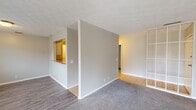 This single-floor residence offers a practical and comfortable layout designed for everyday living. The spacious living area is finished with plush grey carpeting and features a sliding glass door fitted with vertical blinds, allowing natural light to fill the room while providing access to an outdoor patio. A textured ceiling adds visual character throughout the space. An open pass-through connects the living area to the kitchen, which is outfitted with white cabinetry, speckled countertops, and black appliances including an electric range and a full-size refrigerator. Tile flooring runs through the kitchen and into the hallway, creating a clean transition between spaces. The unit includes multiple carpeted bedrooms, each featuring windows with blinds that invite natural light and views of the surroundings. A mirrored partition wall adds a distinctive touch to one of the bedroom areas. The two bathrooms are well-appointed, each with a vanity featuring speckled countertops and a medicine cabinet with lighted mirror. One bathroom includes a tub-shower combination with tile surround and wood-look flooring. Neutral grey tones and white trim carry consistently throughout, giving the entire unit a cohesive and clean aesthetic.