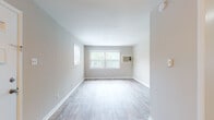 Located at 1414 Poplar Ave in Murfreesboro, Tennessee, this single-floor home offers a clean, straightforward layout with a neutral color palette throughout. The living areas feature light-toned laminate flooring and soft gray walls, creating a bright and airy atmosphere. Large windows allow generous natural light to fill the main living space, which also includes a wall-mounted AC unit for climate control. A front entry door with decorative glass panels provides a welcoming point of arrival, flanked by an additional window that further brightens the area. The kitchen is fitted with warm wood cabinetry in an L-shaped configuration, a double sink, dark countertops, and includes a full-size refrigerator — a practical and functional space for everyday use. The bathroom features classic tiled walls surrounding a full soaking tub with shower, a vanity with storage, and wood-look flooring for a clean finish. The bedroom is carpeted for comfort, includes a ceiling light fixture, and benefits from a window overlooking the outdoors. Throughout the home, consistent white trim and baseboards tie each room together, contributing to a cohesive, well-maintained interior well-suited for comfortable everyday living.